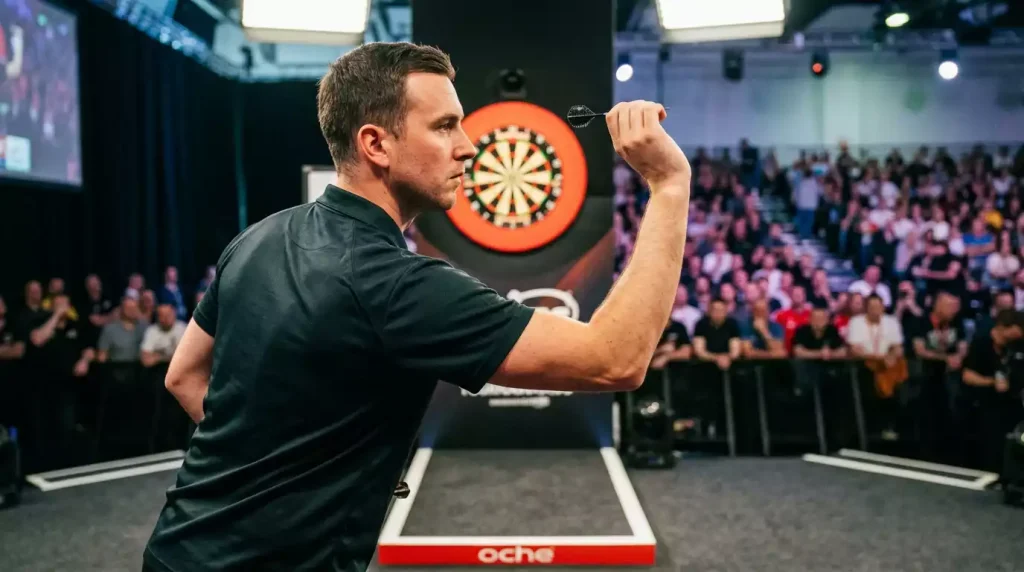 Darts-Profi in fokussierter Wurfhaltung mit beleuchteter Bühne im Hintergrund